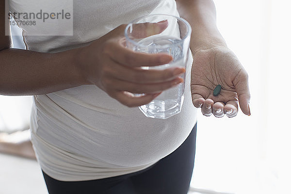 Nahaufnahme einer schwangeren Frau  die ein Vitamin mit Wasser einnimmt