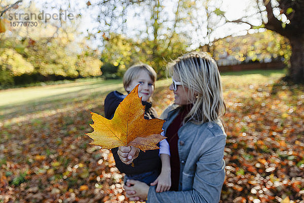 Portrait Mutter und Sohn mit Herbstblatt im sonnigen Park