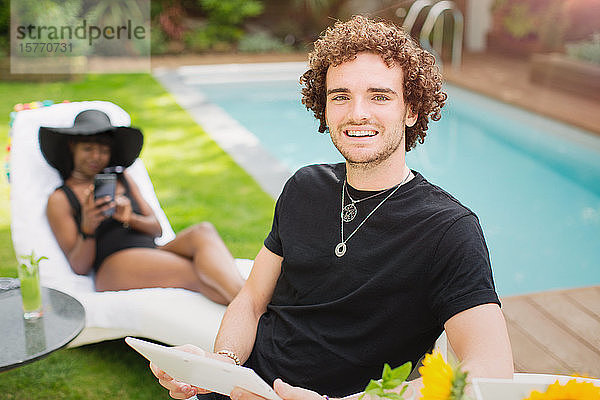 Porträt glücklicher junger Mann mit digitalem Tablet am Swimmingpool