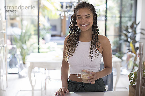 Porträt einer glücklichen jungen Frau  die in der Küche Kaffee trinkt