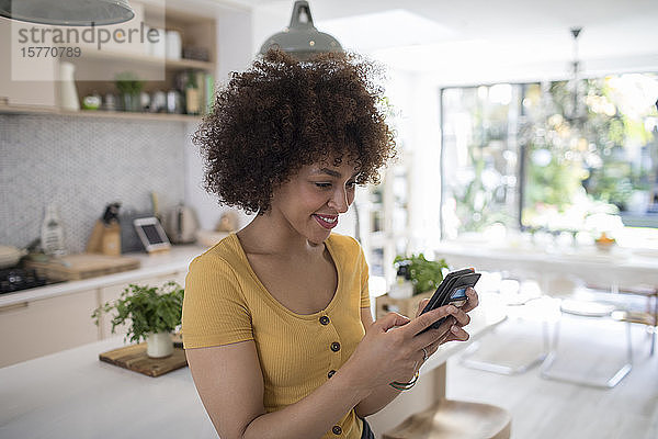 Lächelnde junge Frau benutzt ihr Smartphone in der Küche