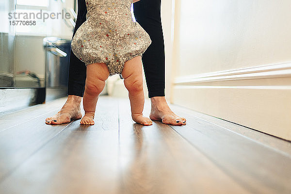 Mutter mit niedrigem Ausschnitt hilft ihrer kleinen Tochter beim Gehen im Korridor