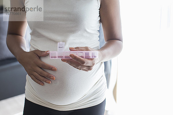 Nahaufnahme einer schwangeren Frau mit Pillenschachtel  die Vitamine einnimmt
