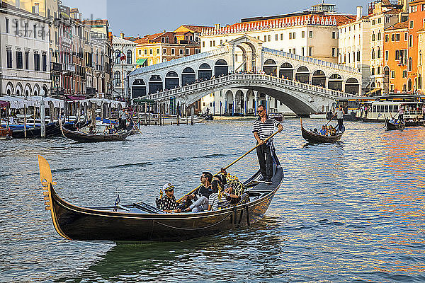 Gondeln und Gondoliere auf dem Canal Grande mit Touristen entlang der bunten Uferpromenade; Venedig  Italien