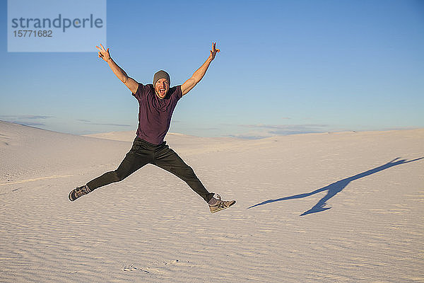 Unbeschwerter Mann in der Luft auf dem weißen Sand mit blauem Himmel  der einen Schatten neben ihn wirft  White Sands National Monument; Alamogordo  New Mexico  Vereinigte Staaten von Amerika