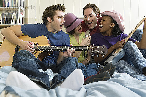 Zwei Männer und zwei Frauen spielen Gitarren im Schlafzimmer.