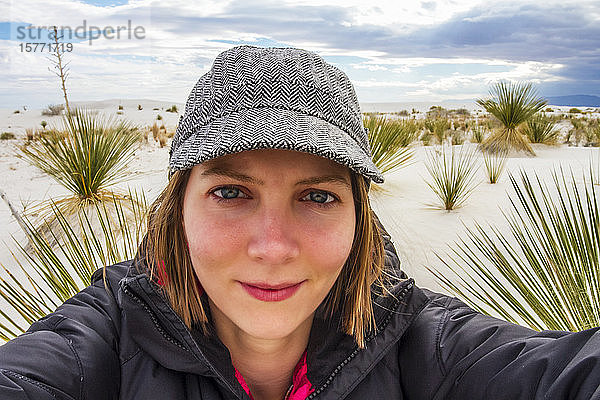 Junge Frau bei der Aufnahme eines Selbstporträts mit Wüstenpflanzen und weißem Sand im Hintergrund  White Sands National Monument; Alamogordo  New Mexico  Vereinigte Staaten von Amerika