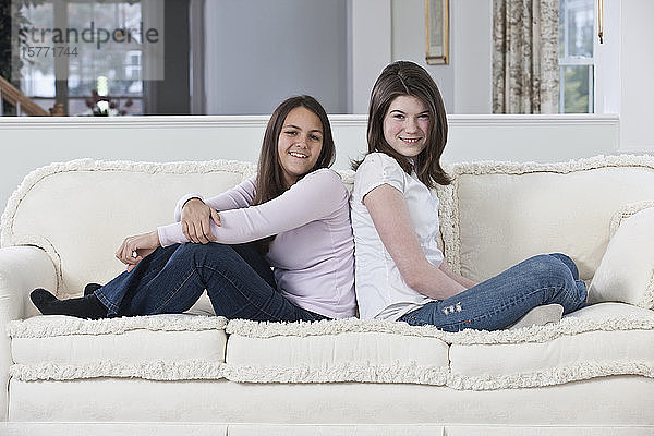 Porträt von zwei Mädchen im Teenageralter  die zu Hause auf einer Couch sitzen