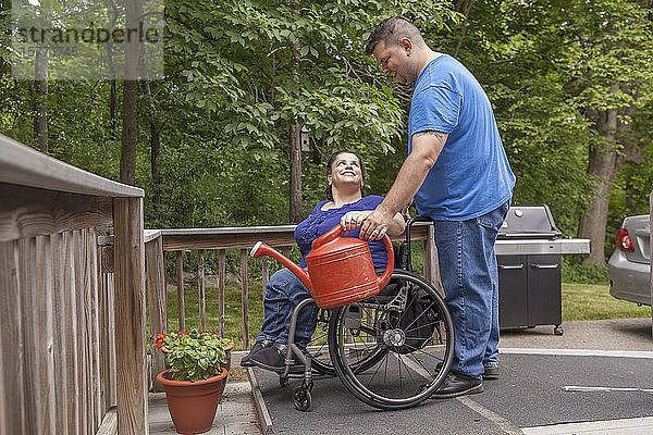 Ein Paar gießt gemeinsam Pflanzen im Garten  wobei die Frau im Rollstuhl sitzt