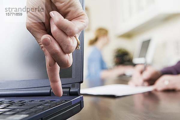 Der Finger einer Frau zeigt nach unten auf eine Taste auf einer Laptop-Tastatur