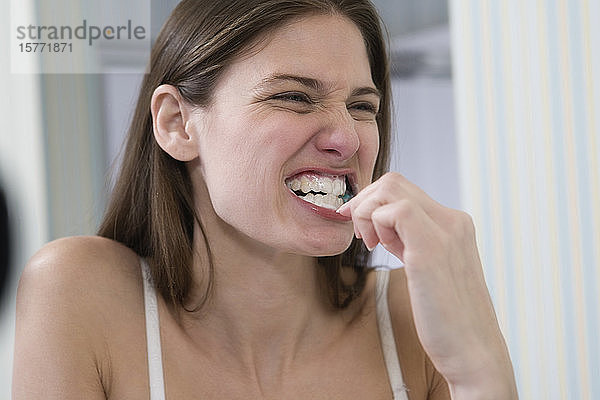 Eine junge Frau putzt sich vor dem Spiegel die Zähne.