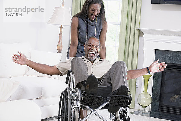 Frau mittleren Alters  die einen Mann mittleren Alters  der in einem Rollstuhl sitzt  lächelnd nach unten schiebt