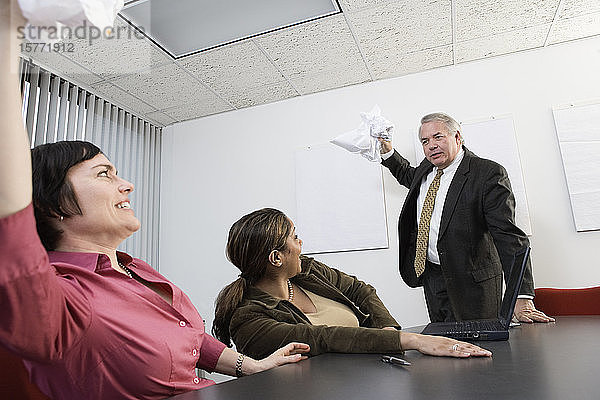 Geschäftsleute  die sich in einem Konferenzraum gegenseitig mit Papieren bewerfen.