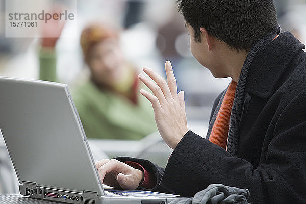 Seitenprofil eines jungen Mannes  der einen Laptop benutzt und mit der Hand winkt