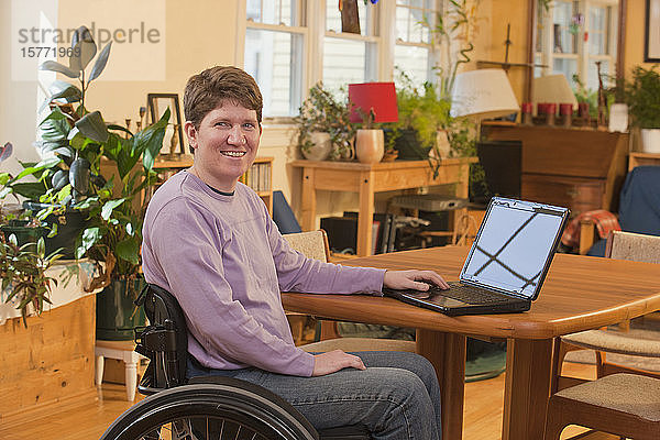Behinderte Person im Rollstuhl  die zu Hause einen Laptop benutzt