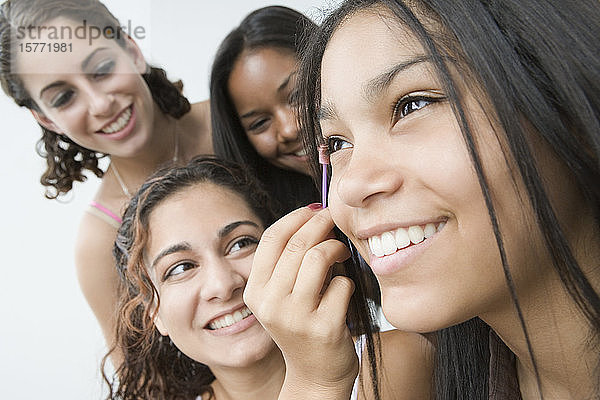 Nahaufnahme einer Teenagerin  die sich die Wimperntusche aufs Auge aufträgt  während ihre Freundinnen neben ihr lächeln