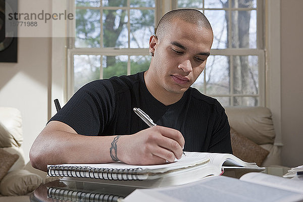 Männlicher Student sitzt zu Hause und macht sich Notizen in einem Notizbuch für Hausaufgaben