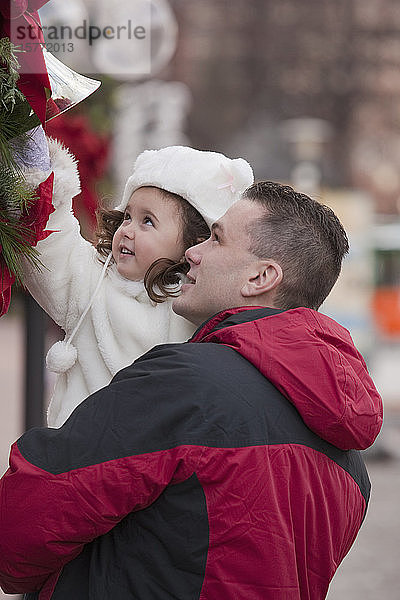 Zeit für den Vater und die kleine Tochter  während er sie im Arm hält und sie nach der Weihnachtsdekoration greift