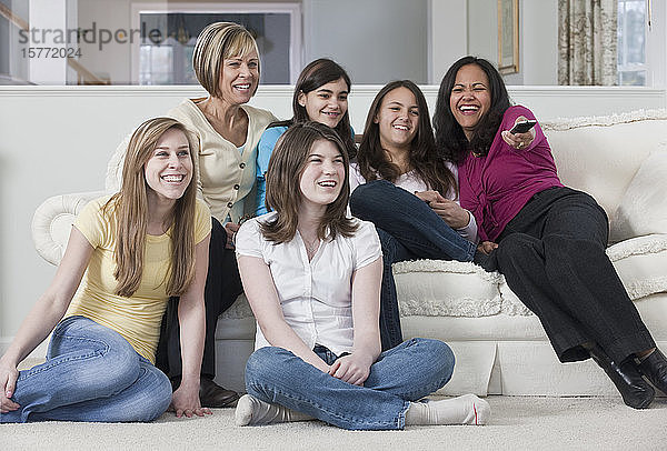 Zwei Mütter mit vier Mädchen im Teenageralter beim Fernsehen