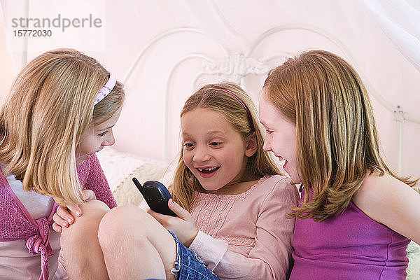 Blick auf drei süße Mädchen  die auf ein Handy schauen.