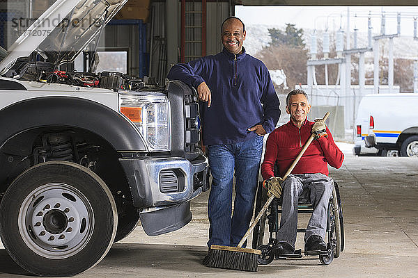 Fahrzeugmechaniker und Mann im Rollstuhl mit Besen posieren für ein Foto
