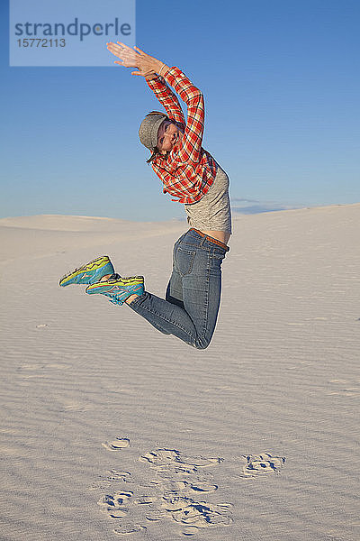 Eine junge Frau springt in die Luft auf dem weißen Sand mit blauem Himmel  White Sands National Monument; Alamogordo  New Mexico  Vereinigte Staaten von Amerika