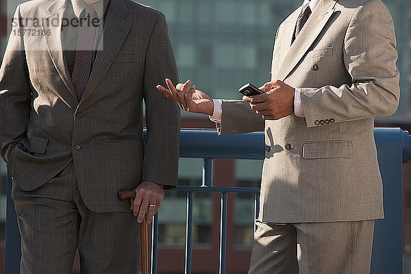 Geschäftsleute stehen zusammen  einer hält einen Stock und einer ein Smartphone