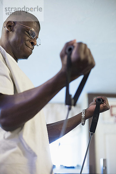 Junger Mann afrikanischer Abstammung  der an einem Gerät seine Arm- und Rumpfkraft trainiert