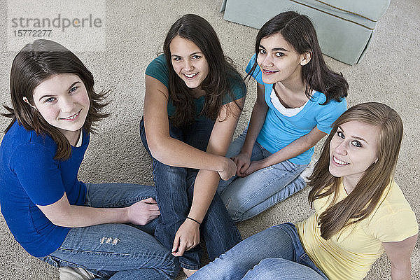 Porträt von vier Mädchen im Teenageralter  die zu Hause auf dem Boden sitzen und in die Kamera schauen