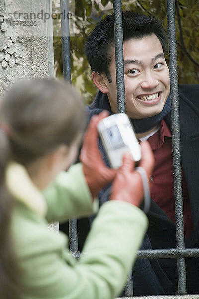 Rückansicht einer jungen Frau  die ihre Freundin hinter einem Sicherheitsgitter fotografiert