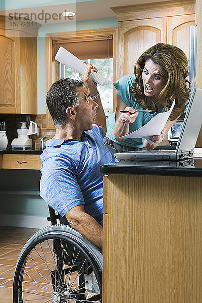 Mittlere erwachsene Frau schreit einen mittleren erwachsenen Mann an  der in einem Rollstuhl sitzt