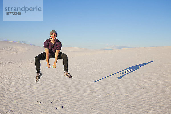 Unbeschwerter Mann in der Luft auf dem weißen Sand mit blauem Himmel  der einen Schatten neben ihn wirft  White Sands National Monument; Alamogordo  New Mexico  Vereinigte Staaten von Amerika