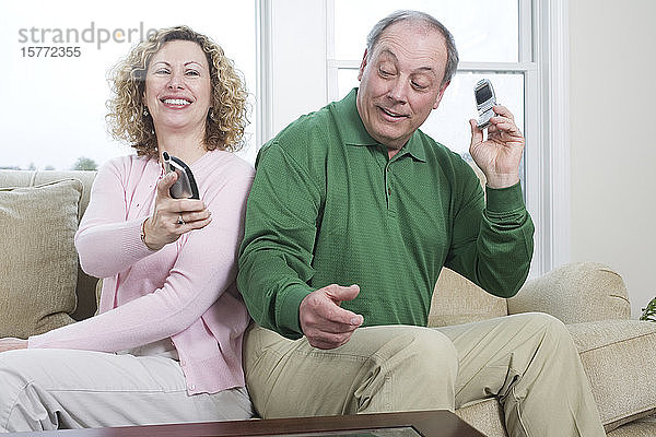 Blick auf ein älteres Paar  das Rücken an Rücken mit Mobiltelefonen und Schnurlostelefonen sitzt.