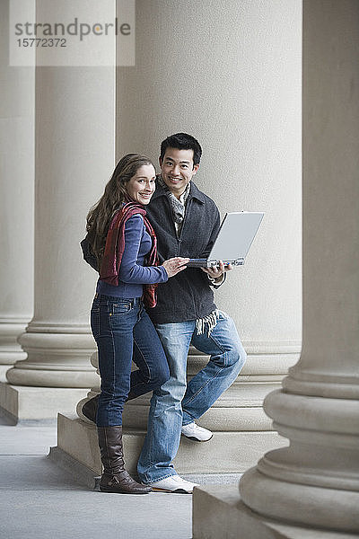 Porträt eines jungen Mannes  der einen Laptop hält und mit einer jungen Frau steht