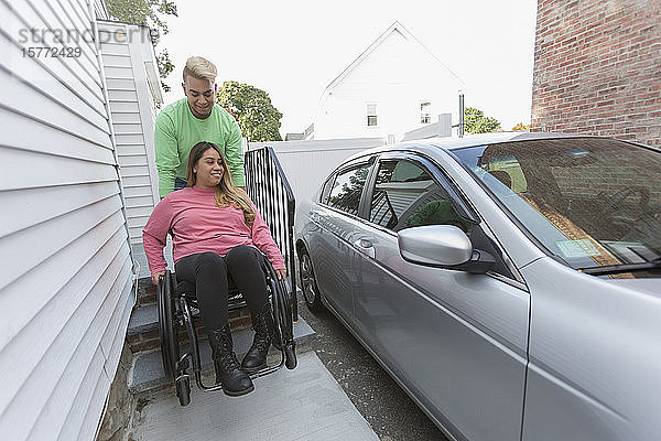 Mann hilft einer Frau mit einer Rückenmarksverletzung beim Einsteigen in ihr Auto