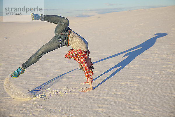 Eine junge Frau macht eine akrobatische Bewegung auf dem weißen Sand mit blauem Himmel  White Sands National Monument; Alamogordo  New Mexico  Vereinigte Staaten von Amerika