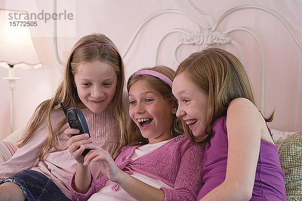 Blick auf drei süße Mädchen  die ein Handy halten.