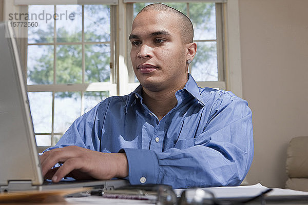Junger Mann  der von zu Hause aus an einem Tisch mit seinem Laptop-Computer arbeitet
