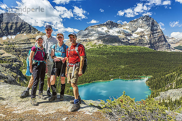 Zwei Paare von Wanderern stehen auf einem felsigen Grat mit einem blauen Alpensee und Bergen in der Ferne mit blauem Himmel und Wolken  Yoho National Park; Field  British Columbia  Kanada