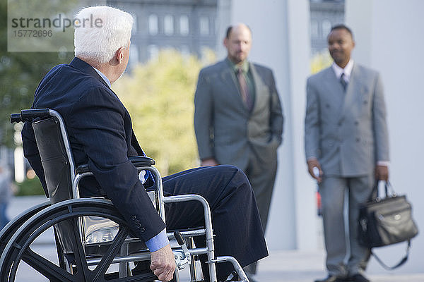 Lächelnder Geschäftsmann im Rollstuhl  zwei Kollegen im Hintergrund