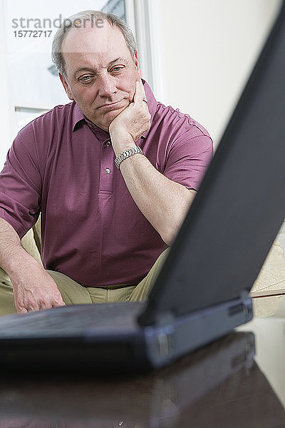 Blick auf einen verwirrten Mann  der auf einen Laptop schaut.