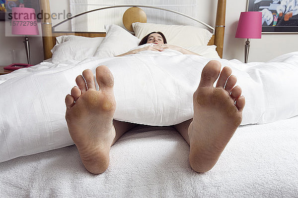 Junge Frau schläft in einem Schlafzimmer und zeigt ihre Füße.