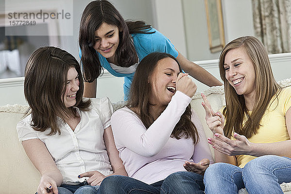 Vier Mädchen im Teenageralter sitzen zu Hause auf einer Couch und spielen das Spiel Stein  Papier  Schere