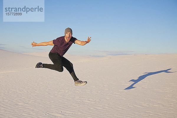 Unbeschwerter Mann in der Luft auf dem weißen Sand mit blauem Himmel  der einen Schatten neben ihn wirft  White Sands National Monument; Alamogordo  New Mexico  Vereinigte Staaten von Amerika