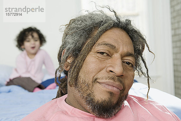 Porträt eines lächelnden erwachsenen Mannes mit seiner hinter ihm sitzenden Tochter