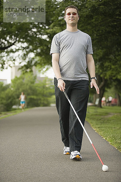 Mann  der mit einem Blindenstock auf einem Gehweg geht