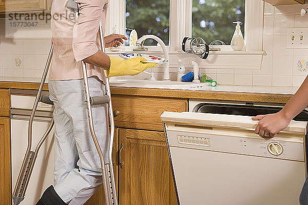 Mittelaufnahme einer Frau mittleren Alters  die in der Küche steht und Geschirr spült