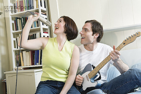 Mann mit Gitarre und Frau mit Mikrofon im Schlafzimmer.