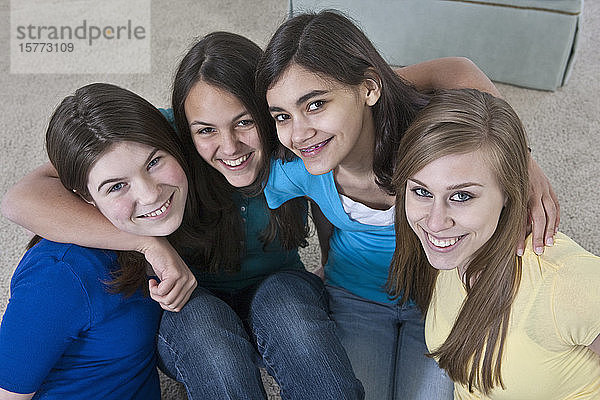 Porträt von vier Mädchen im Teenageralter  die zu Hause auf dem Boden sitzen und in die Kamera blicken