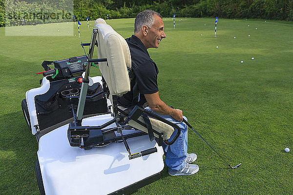 Ein behinderter Mann sitzt in einem angepassten Rollstuhl und spielt Golf auf einem Golfplatz